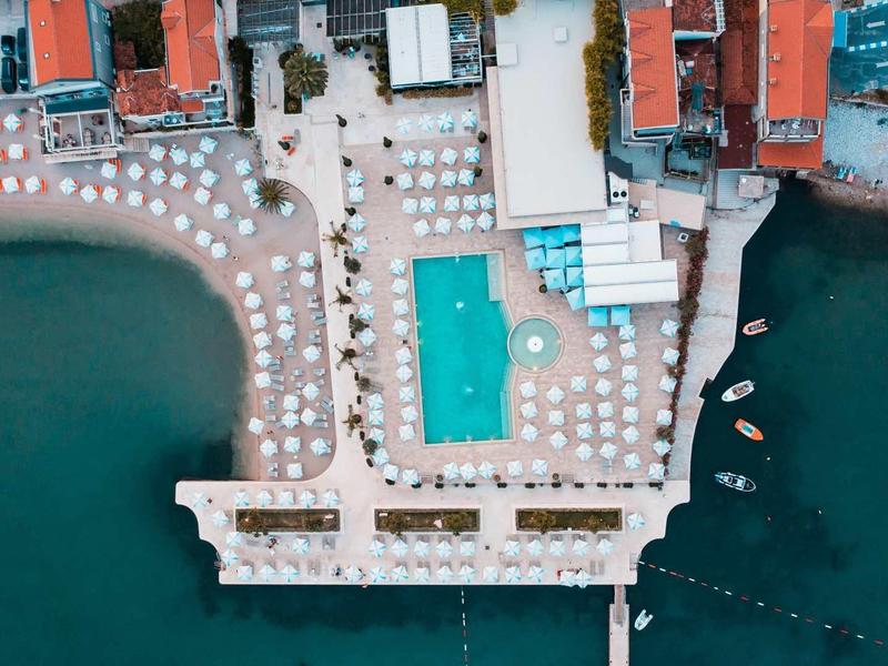 Vista aérea de un hotel con piscina y tumbonas junto al agua turquesa