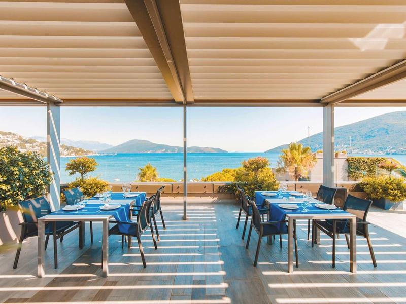 Terraza cubierta con mesas y sillas con vistas al mar y las montañas.