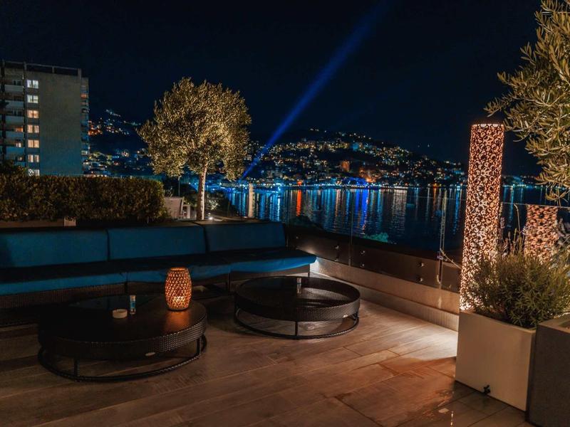 Terraza exterior acogedora con iluminación y vista al lago iluminado de noche.