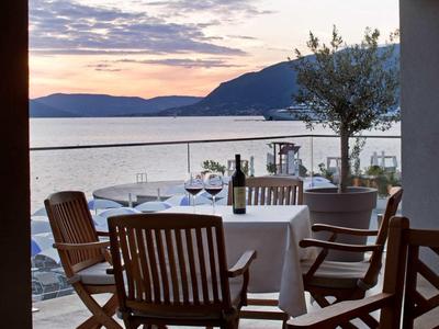 Een gedekte tafel met stoelen op een terras met uitzicht op zee en bergen bij zonsondergang.
