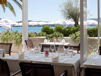 Terrassenrestaurant mit gedeckten Tischen und Blick auf das Meer und Sonnenschirme.