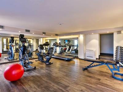 Moderne Fitnessstudio mit verschiedenen Geräten und Hanteln in hellem Raum mit Holzboden.