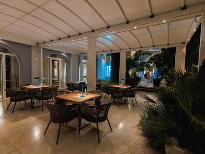 Gemütlicher Außenbereich eines Hotels mit Tischen, Stühlen und Pflanzen unter einer Markise.