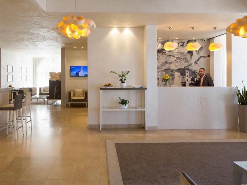 Lichte hotelreceptie met witte balie, moderne verlichting en zitplaatsen.