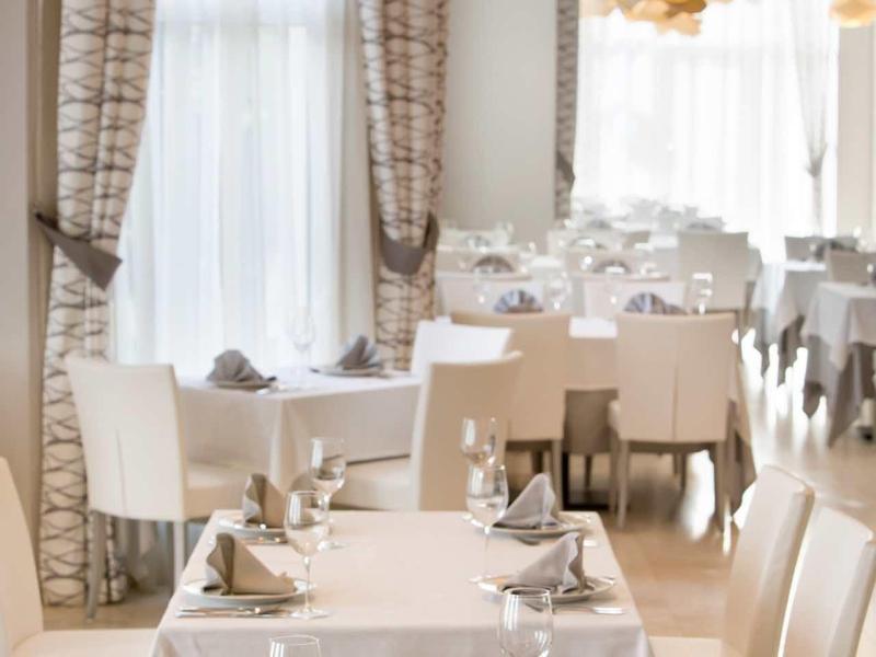 Elegant restaurant met witte tafels en stoelen, grote ramen en moderne gouden plafondlampen.