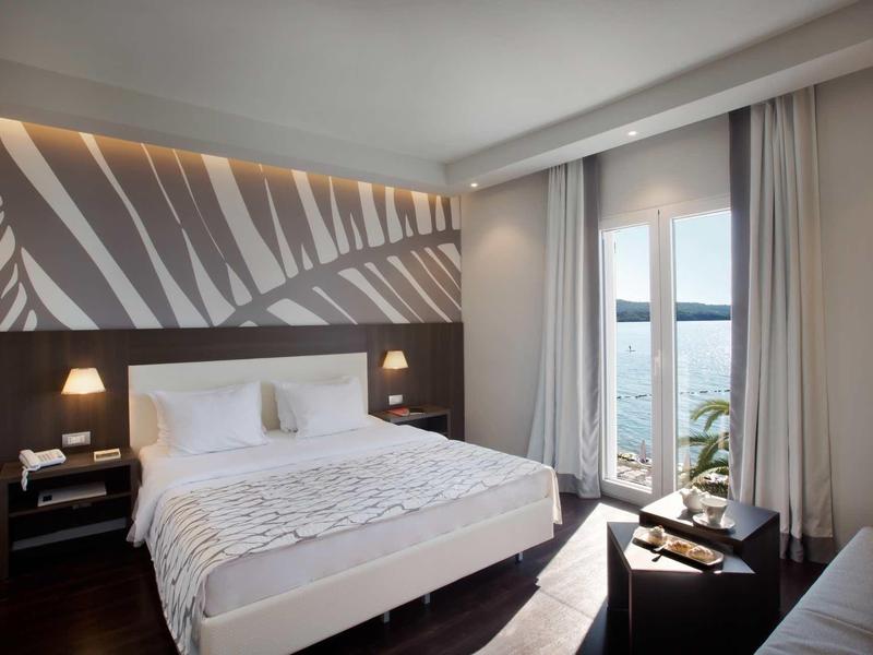 Moderne hotelkamer met groot bed, nachtkastjes en balkon met uitzicht op zee.