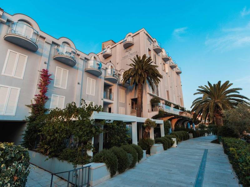 Elegant hotelgebouw met balkons, palmbomen en een brede wandelweg onder een heldere lucht.