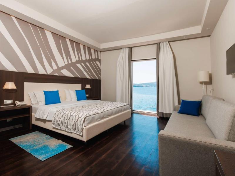 Moderne hotelkamer met tweepersoonsbed, bank, balkon en uitzicht op zee.