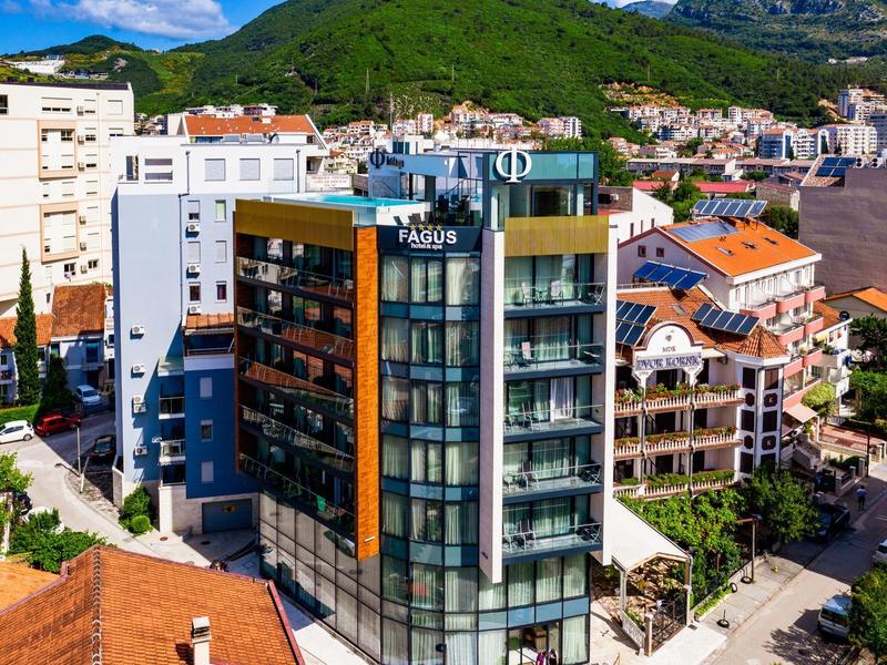 Modern hotel with glass facade in a city with green mountains in the background under sunlight.