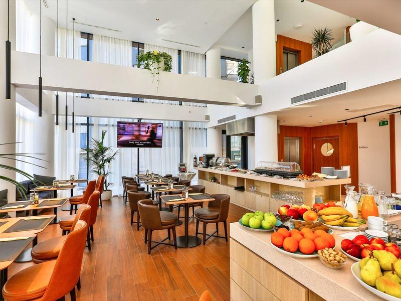 Modern hotel restaurant with buffet, stylish furniture, large windows, and bright colors.
