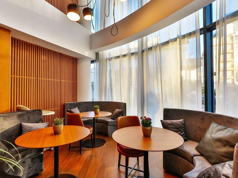 Cozy lounge area with round tables and sofas by large hotel windows.