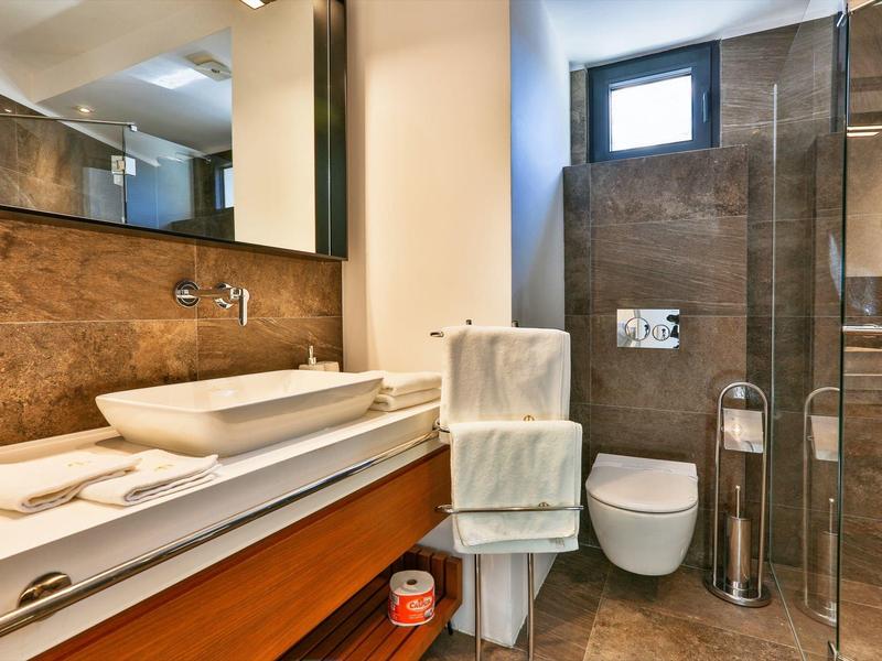 Modern hotel bathroom with sink, toilet, and towels on brown tiled walls.