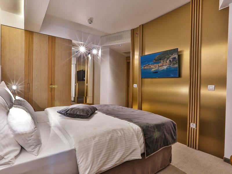 Modern hotel room with double bed, white pillows, brown bedspread, and wall art.