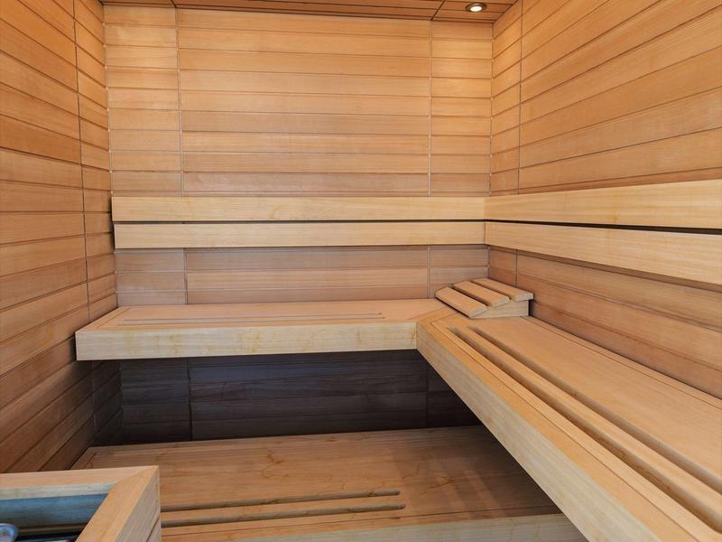 Interior view of a bright wooden sauna with multi-level seating and indirect lighting.