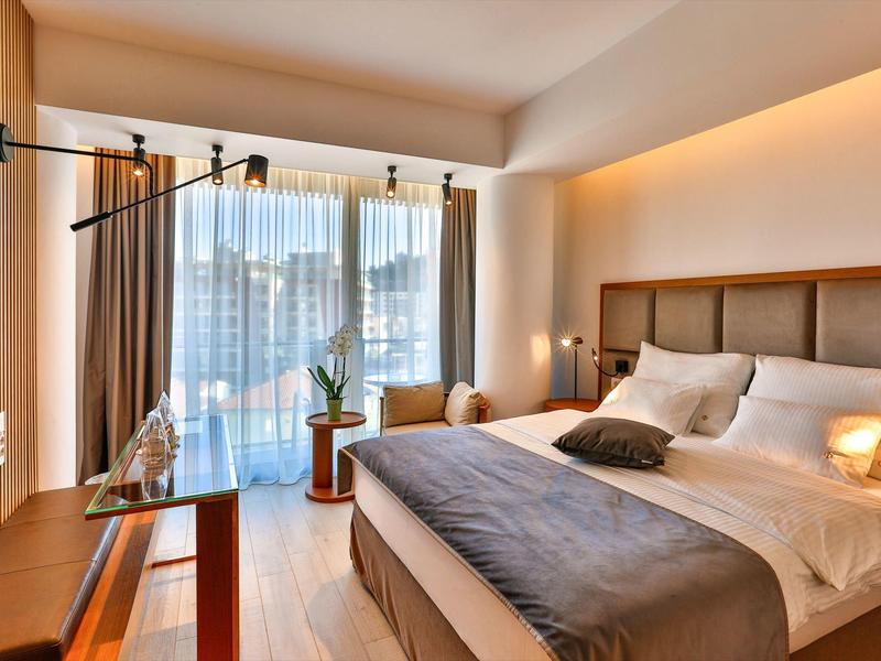 Modern hotel room with large double bed, TV, and balcony with view.