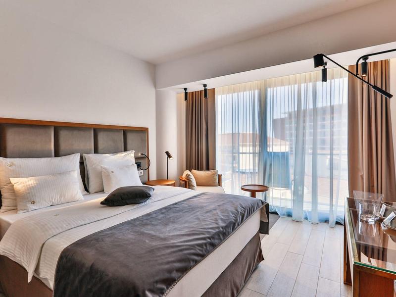 Modern hotel room with large bed, desk, and balcony with curtains