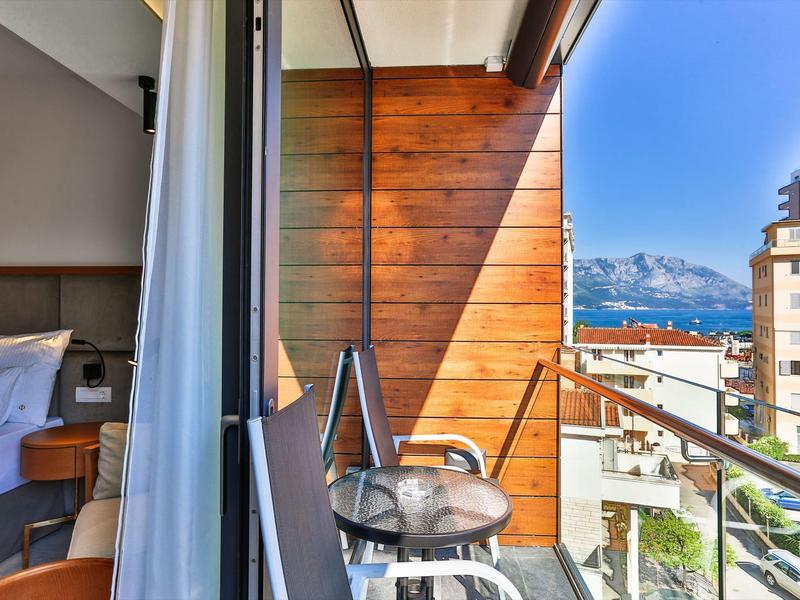 Balcony with chairs and table overlooking city, sea, and mountains under clear sky.