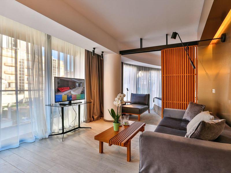 Modern living room with sofa, TV, and large window with curtains.