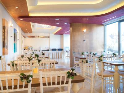 Helles Restaurant mit weißen Stühlen, gedeckten Tischen und moderner Beleuchtung.