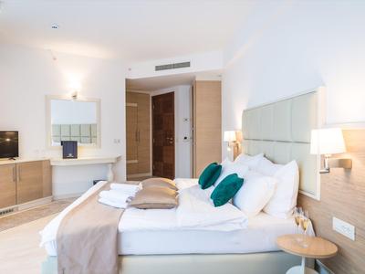 Modernes Hotelzimmer mit großem Bett, weißen Wänden und Holzmöbeln, hell und einladend.