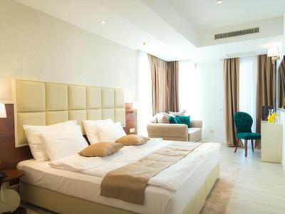 Bright hotel room with large bed, seating area, and windows with curtains.