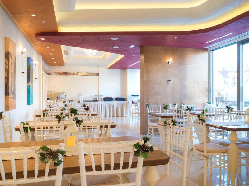 Brightly lit hotel dining area with white chairs and tables.