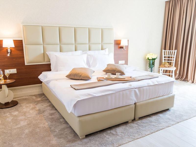 Bright hotel room with spacious double bed, wood accents, and daylight from curtains.