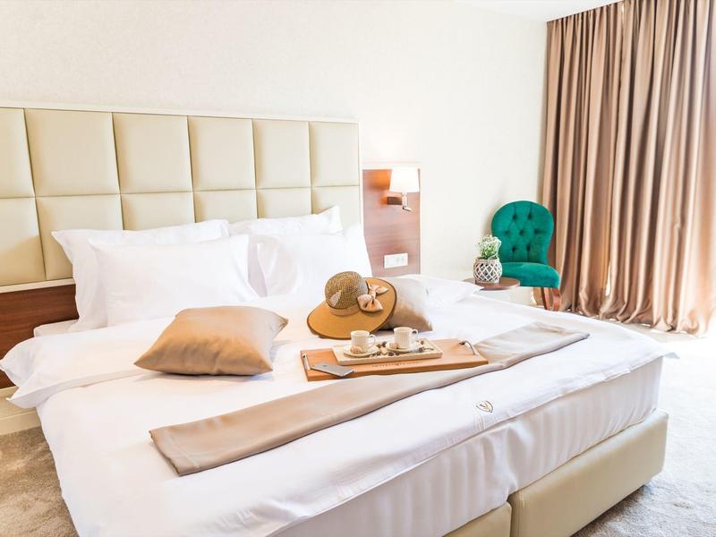 Bright hotel room with large bed, decorative pillows, and breakfast on a tray.