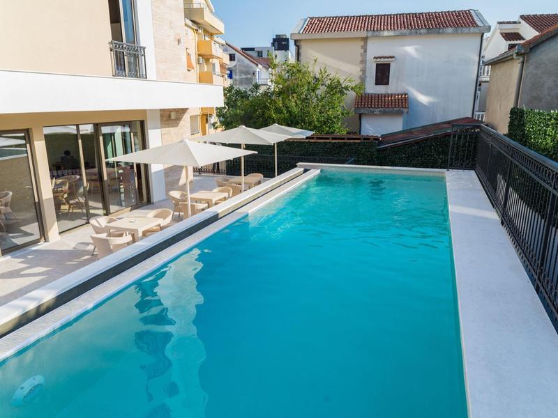Modern outdoor pool beside a white building with umbrellas and lounge chairs.