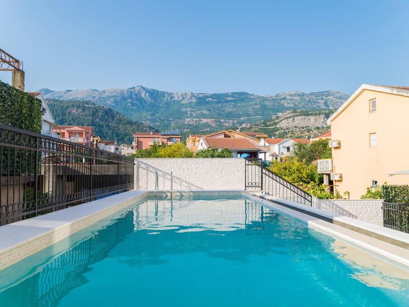Small swimming pool with clear water in front of houses and mountains under clear sky.