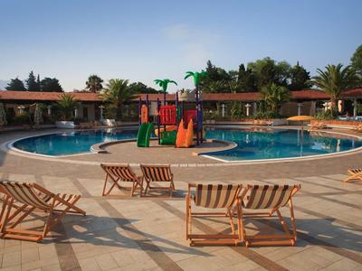 Piscina redonda grande con juegos de agua y tumbonas bajo cielo azul en un resort hotelero.