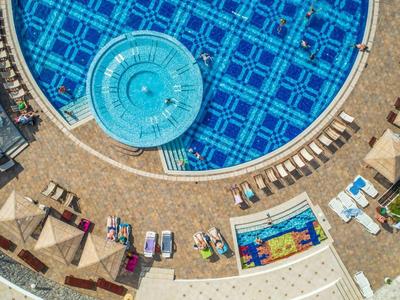 Luftaufnahme eines großen runden Pools mit Sonnenschirmen und Liegestühlen am Rand.