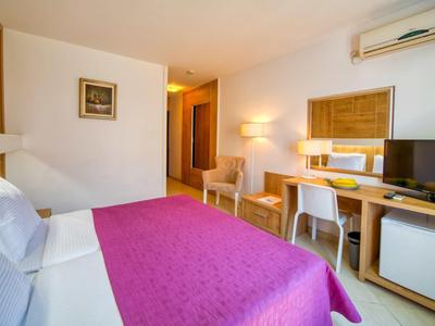 Habitación de hotel con cama grande, manta morada, escritorio, tv y aire acondicionado en la pared.