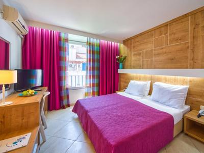 Acogedora habitación de hotel con cama doble, cubrecama rosa y pared de madera detrás de la cama.