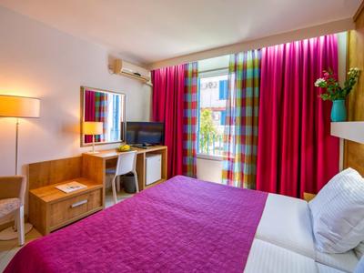 Acogedora habitación de hotel con cama doble, colcha y cortinas rojas, escritorio y televisor.