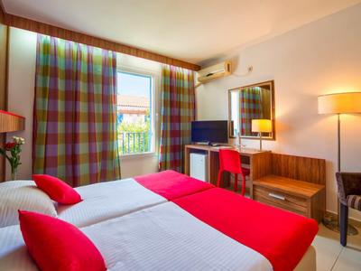 Habitación de hotel luminosa con dos camas individuales, cortinas coloridas y balcón con vista exterior.