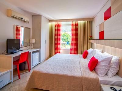 Habitación de hotel moderna con cama doble, acentos rojos y ventana con vista al verde.