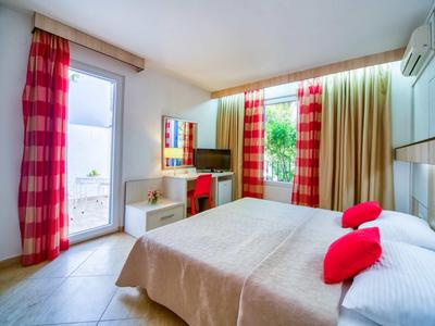 Habitación de hotel luminosa con cama doble, cojines rojos, cortinas coloridas y escritorio con espejo.