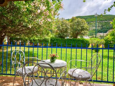 Pequeña mesa y sillas de hierro en un balcón con vista a un jardín verde y montañas.
