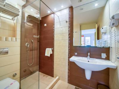 Baño moderno con ducha, lavabo, inodoro y espejos grandes en una habitación de hotel.