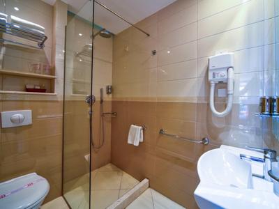 Baño luminoso con ducha de vidrio, lavabo, inodoro y secador de pelo en la pared.