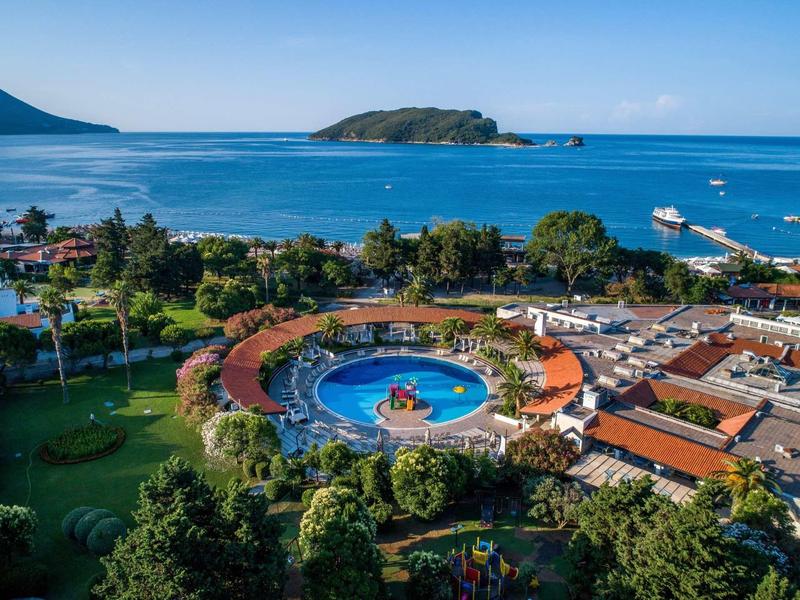 Complejo hotelero con piscina circular, rodeado de áreas verdes y vista al mar con una isla al fondo.