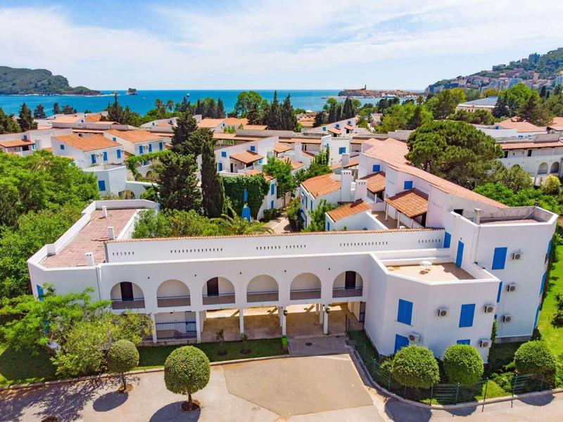 Edificio de hotel blanco con puertas azules y balcones cerca del mar rodeado de árboles.