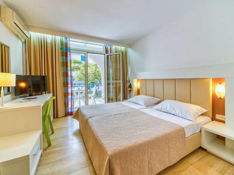 Habitación de hotel luminosa con cama doble, escritorio, televisor y acceso a un balcón.