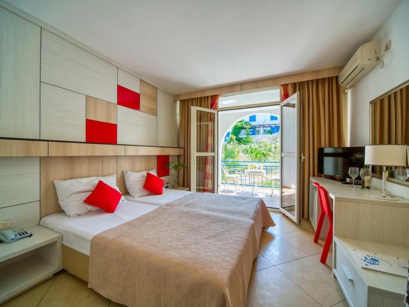 Habitación de hotel luminosa con dos camas, balcón y decoración moderna en rojo y beige.