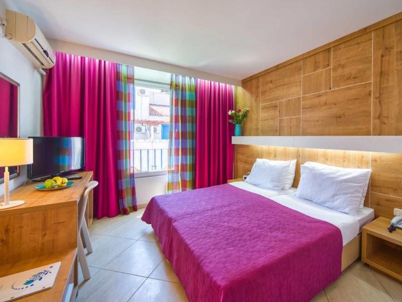 Acogedora habitación de hotel con cama doble, cubrecama rosa y pared de madera detrás de la cama.