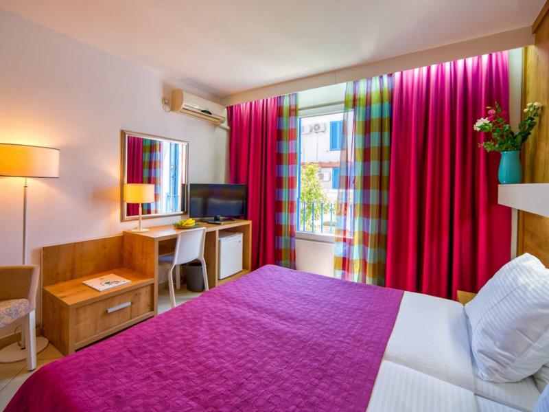 Acogedora habitación de hotel con cama doble, colcha y cortinas rojas, escritorio y televisor.