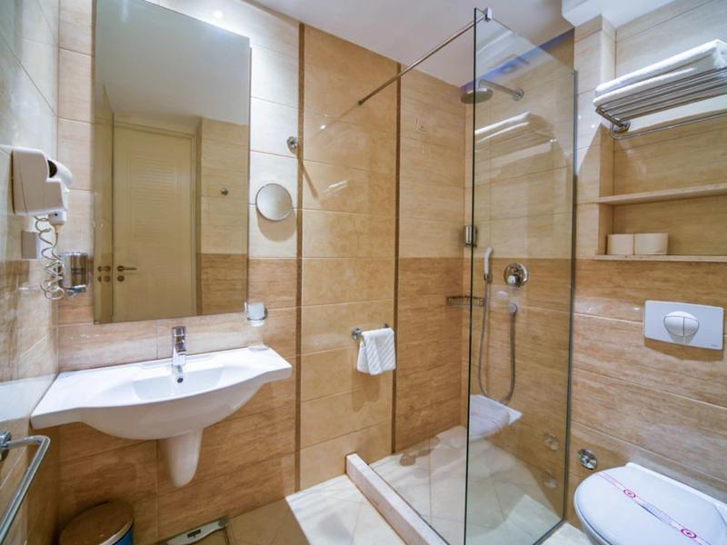 Baño de hotel moderno con espejo grande, ducha de vidrio y lavabo blanco.