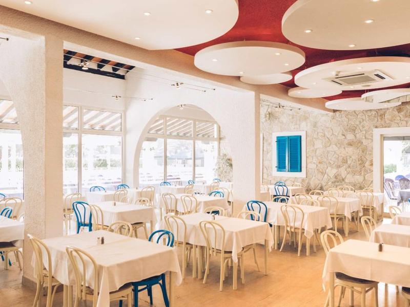 Restaurante luminoso con mesas blancas, sillas mixtas y ventanas con vista al exterior