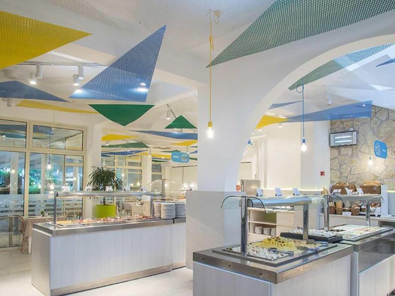 Restaurante moderno con techos altos, decoración colorida y buffet en un espacio luminoso y amplio.